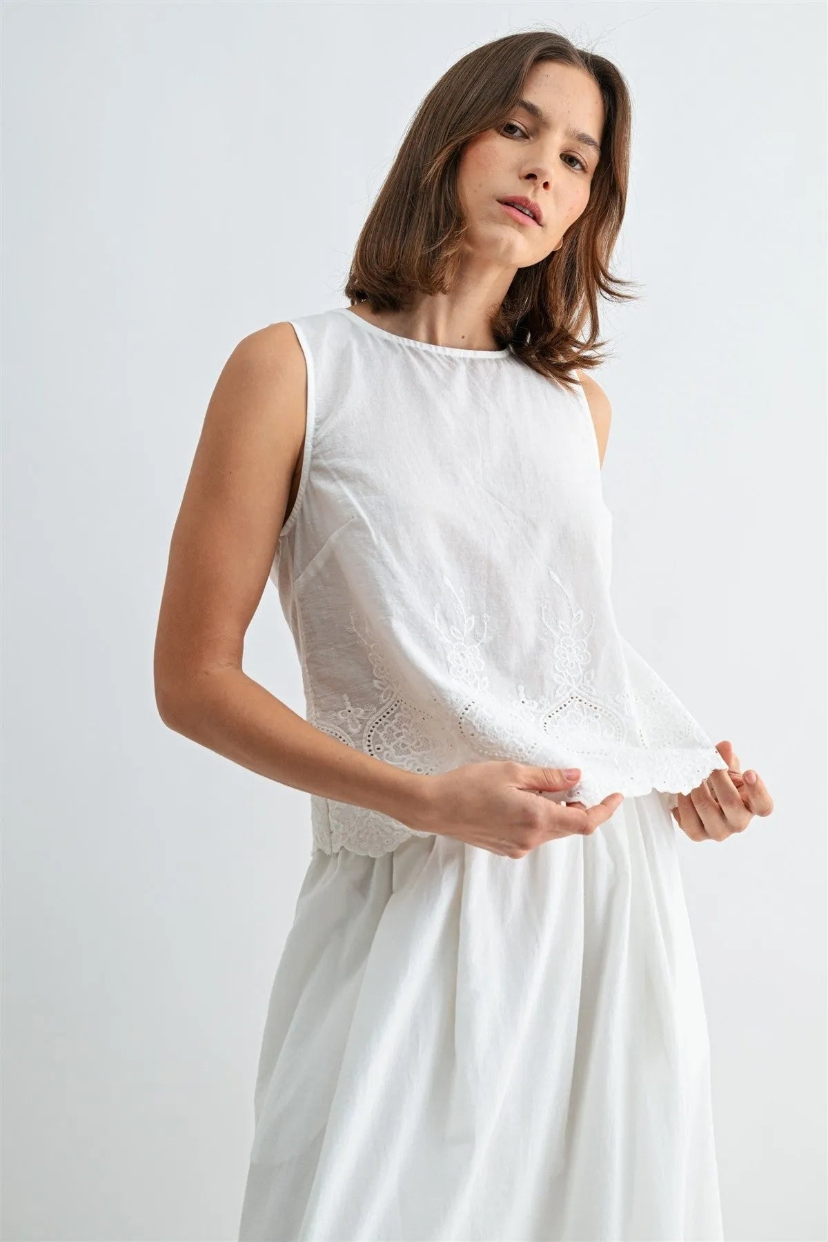 White sleeveless button blouse featuring delicate lace eyelet hem and neckline detailing with back button closure