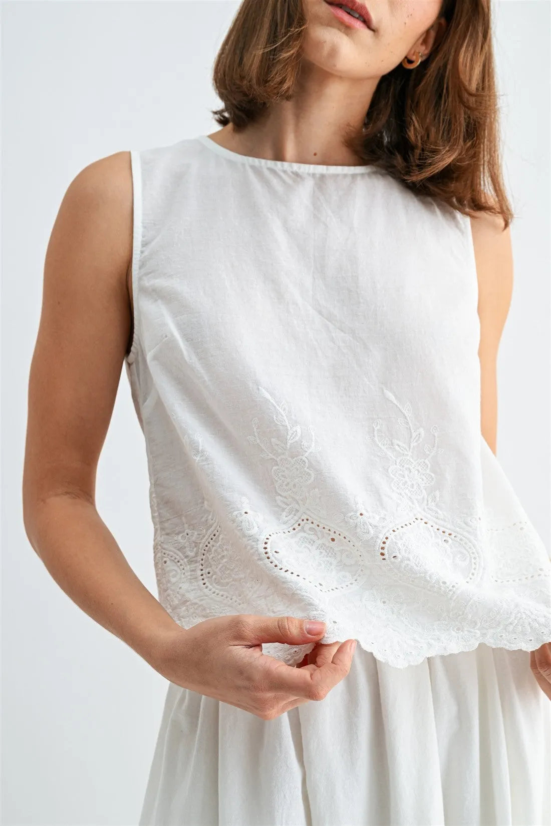 White sleeveless button blouse with delicate lace embroidery and eyelet hem scalloped detailing visible from the back