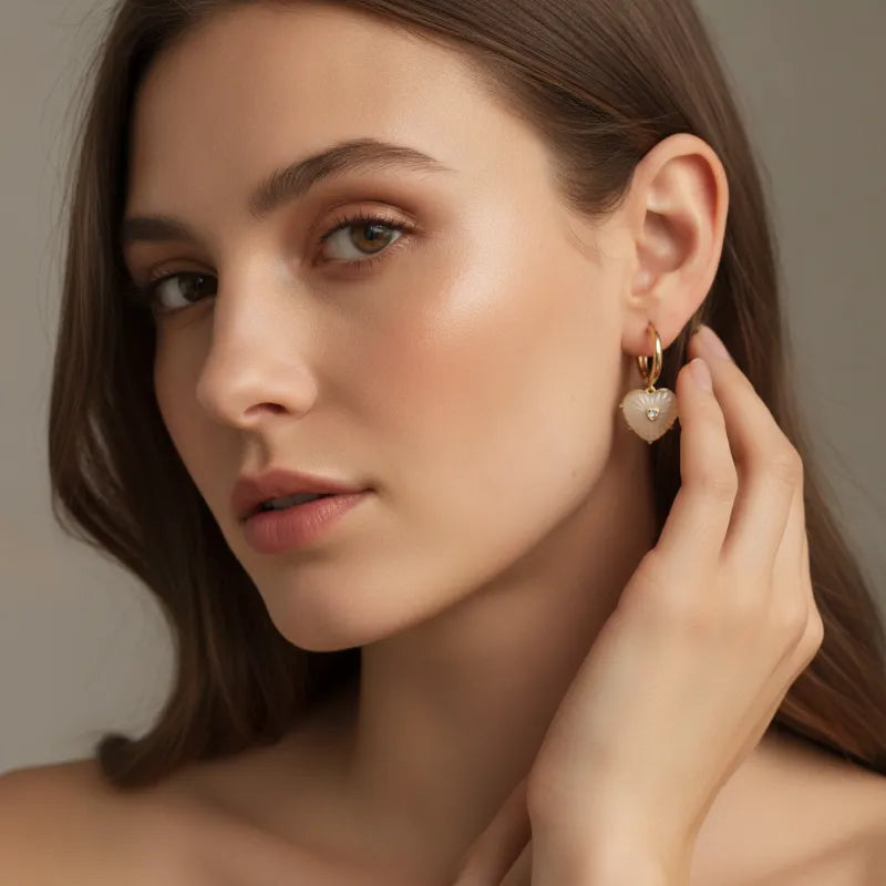 Elegant gold heart hoop earrings featuring a gold hoop with a translucent white heart pendant adorned with peach crystals