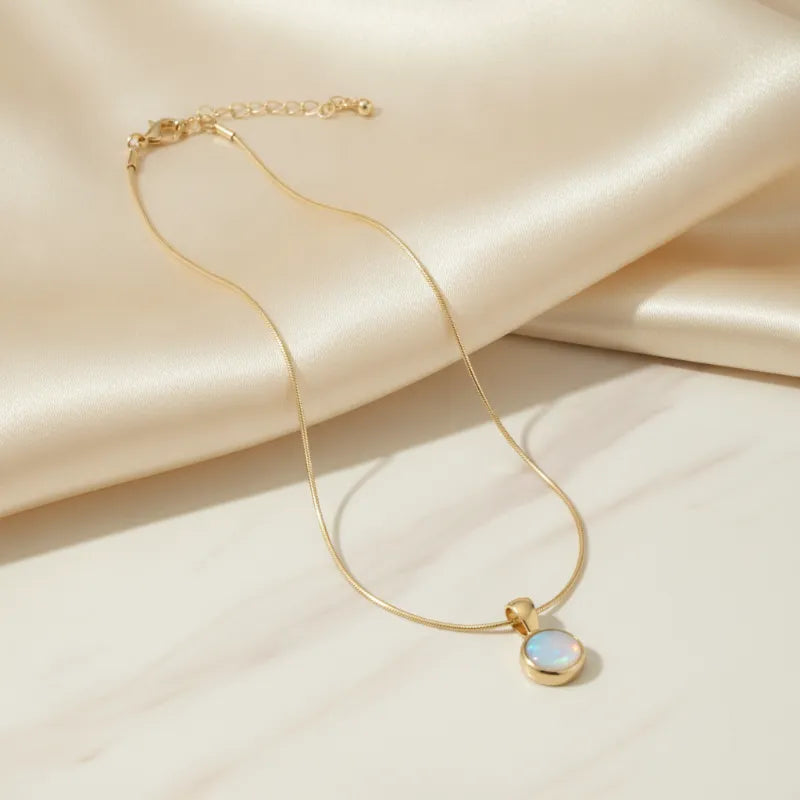 Delicate gold snake chain necklace with a small round mother of pearl pendant in soft blue and white iridescent finish