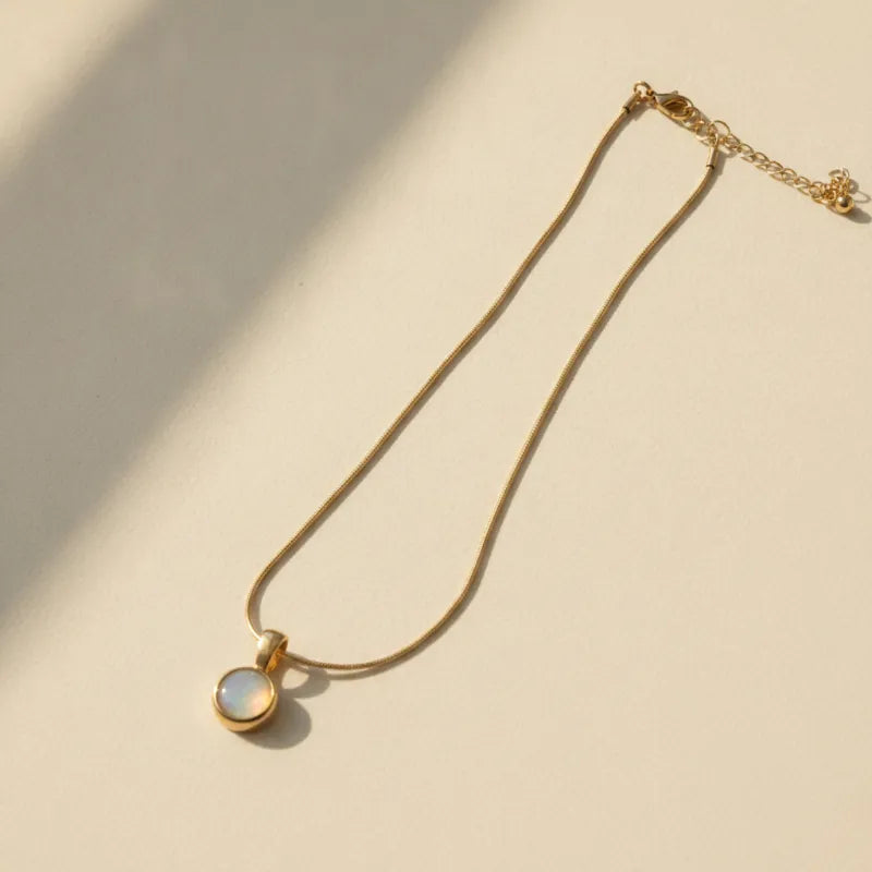 Gold snake chain necklace with round mother of pearl pendant featuring a soft iridescent sheen