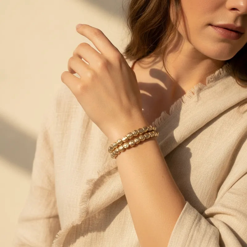 Gold-toned hammered gold stretch bracelet with textured faceted beads worn as a stylish bracelet stack on the wrist