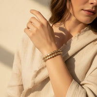 Gold-toned hammered gold stretch bracelet with textured faceted beads worn as a stylish bracelet stack on the wrist