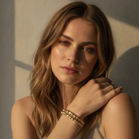 Gold-toned hammered gold stretch bracelet with interlocking links worn as part of a bracelet stack on the wrist