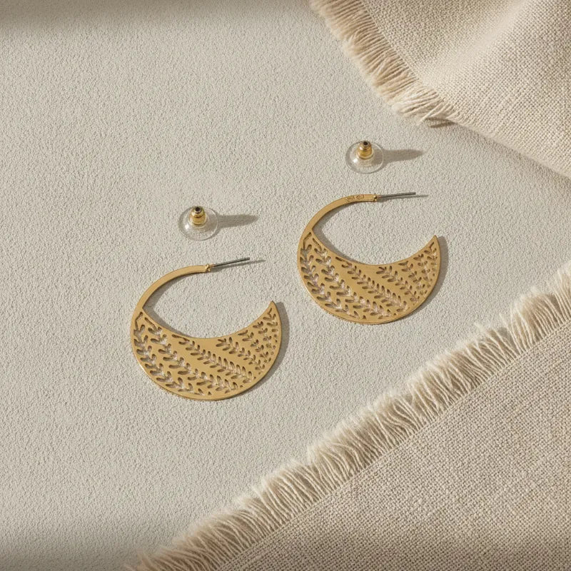 Gold-tone crescent-shaped hoop earrings with intricate botanical cutout design for chic statement jewelry
