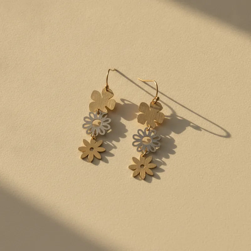 Gold-toned three-tiered floral dangle earrings with layered flower-shaped charms in varying sizes and finishes