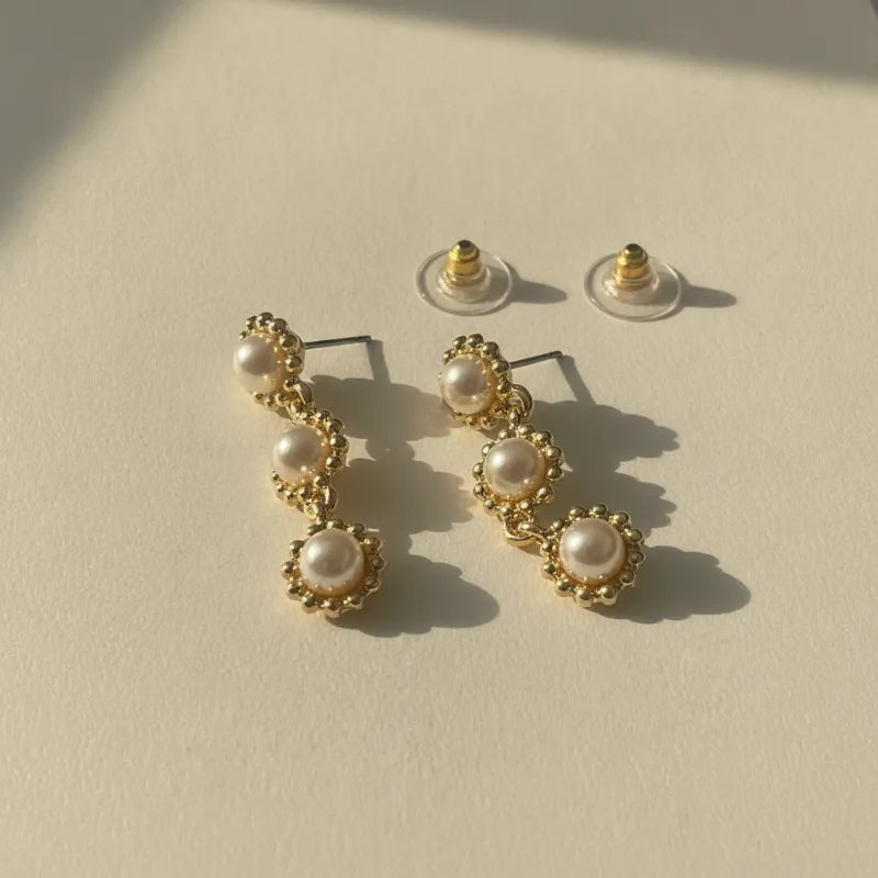 Gold-toned triple pearl dangle earrings featuring three graduated pearls in an elegant floral-inspired design
