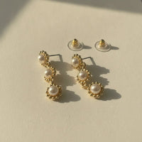 Gold-toned triple pearl dangle earrings featuring three graduated pearls in an elegant floral-inspired design