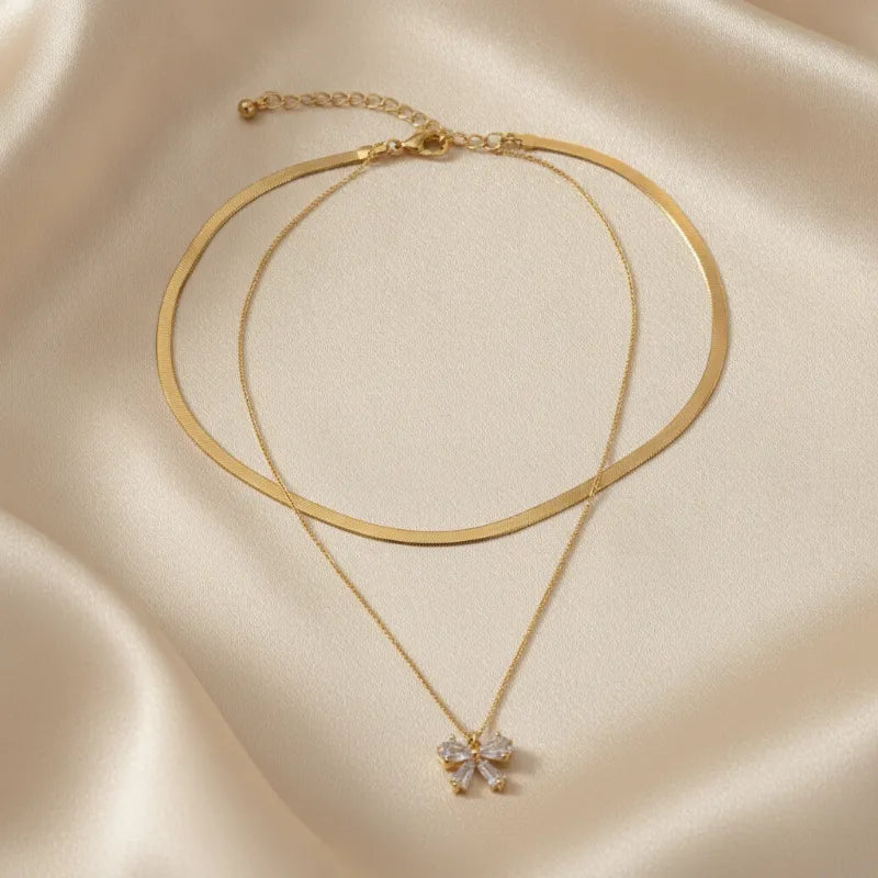 Gold-toned double snake chain choker necklace with double snake layers and a sparkling bow pendant charm