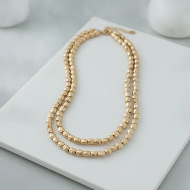 Double-strand matte gold hammered bead statement necklace with a textured hammered finish in gold tone
