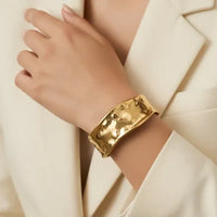 Gold-toned hammered surface water resistant metal cuff bracelet with a wide rectangular design and steel finish