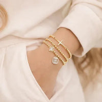 Gold-toned cross beaded stretch bracelet set with layered design featuring cross charm and square-cut crystal pendants