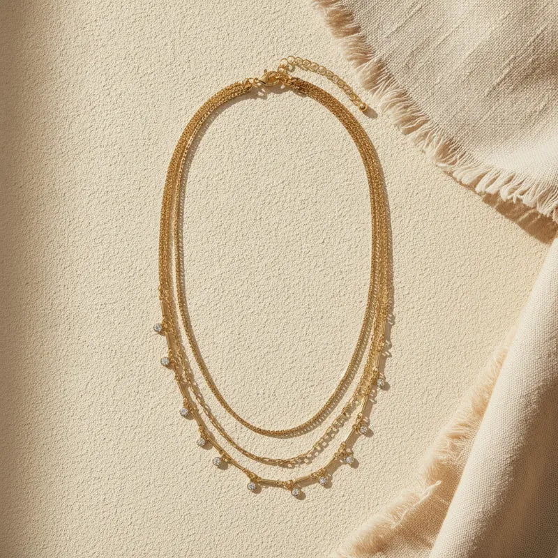 Gold layered necklace with delicate chain links and small pearl-like beads featuring shimmering crystal charms
