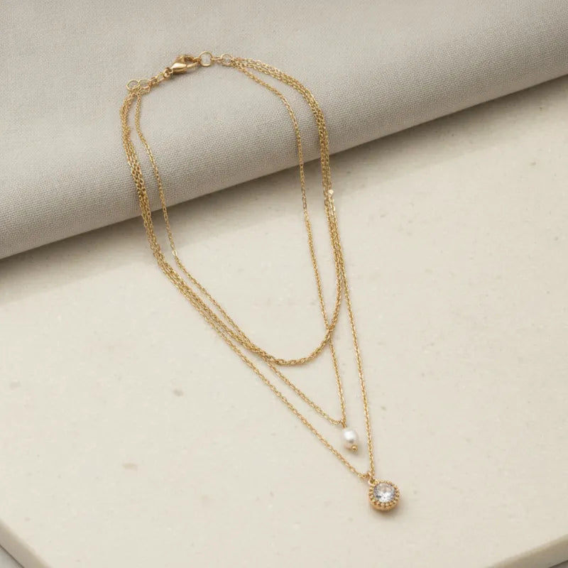 Gold-toned multi-layered chain necklace with pearl drop and round crystal pendant featuring delicate beads