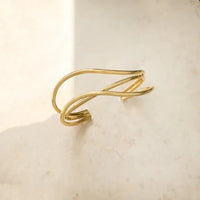 Gold-toned minimalist cuff bracelet featuring a water resistant three curved bands design in sleek intertwined wire