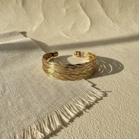 Gold-toned multi-strand woven cuff bracelet with textured braided design and polished spherical clasps golden tide cuff