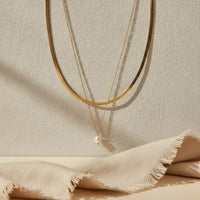 Gold-toned double snake chain necklace with a delicate chain and single pearl pendant charm