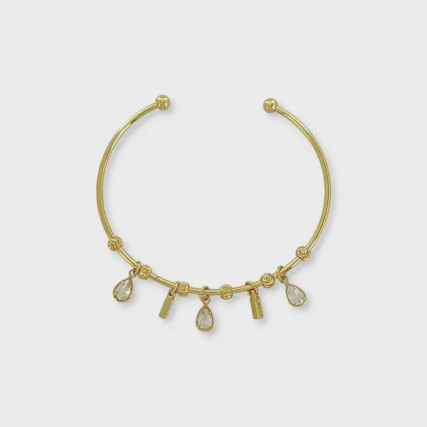 Gold-toned cuff bracelet featuring teardrop cz charm dangles and small cylindrical accents in a charm cuff bracelet design