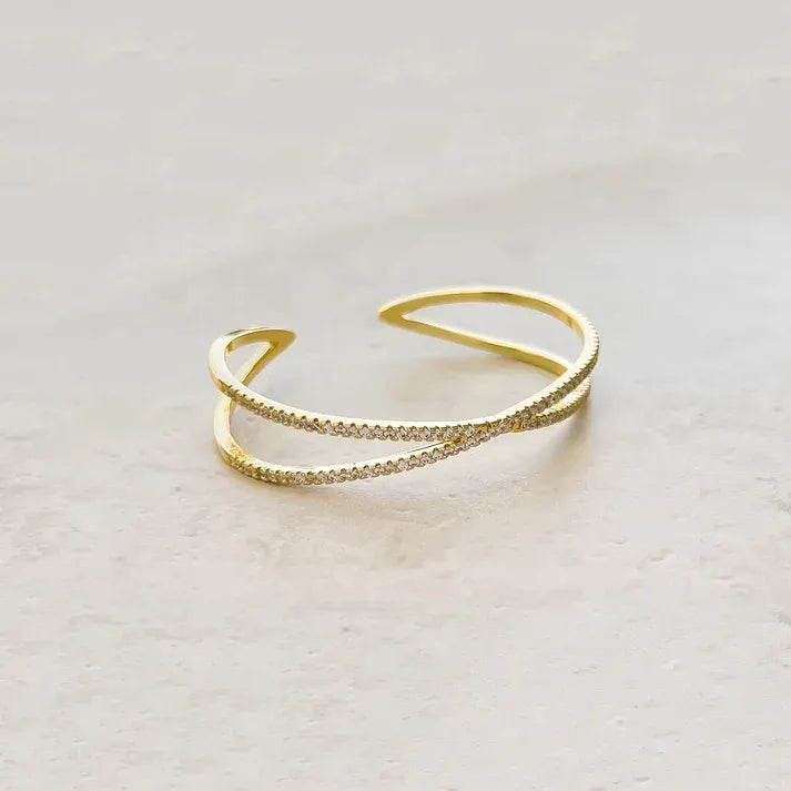 Gold-toned crisscross shape open cuff bracelet with delicate intertwined design and small sparkling stones along edges