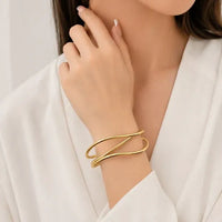 Gold-toned water resistant three curved bands cuff bangle with sleek intersecting design worn on the wrist