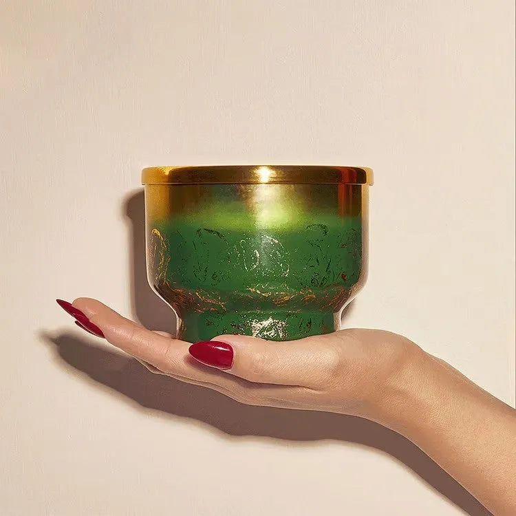 A hand holds a green and gold metallic crystal pine glimmer inverted candle holder with intricate detailing