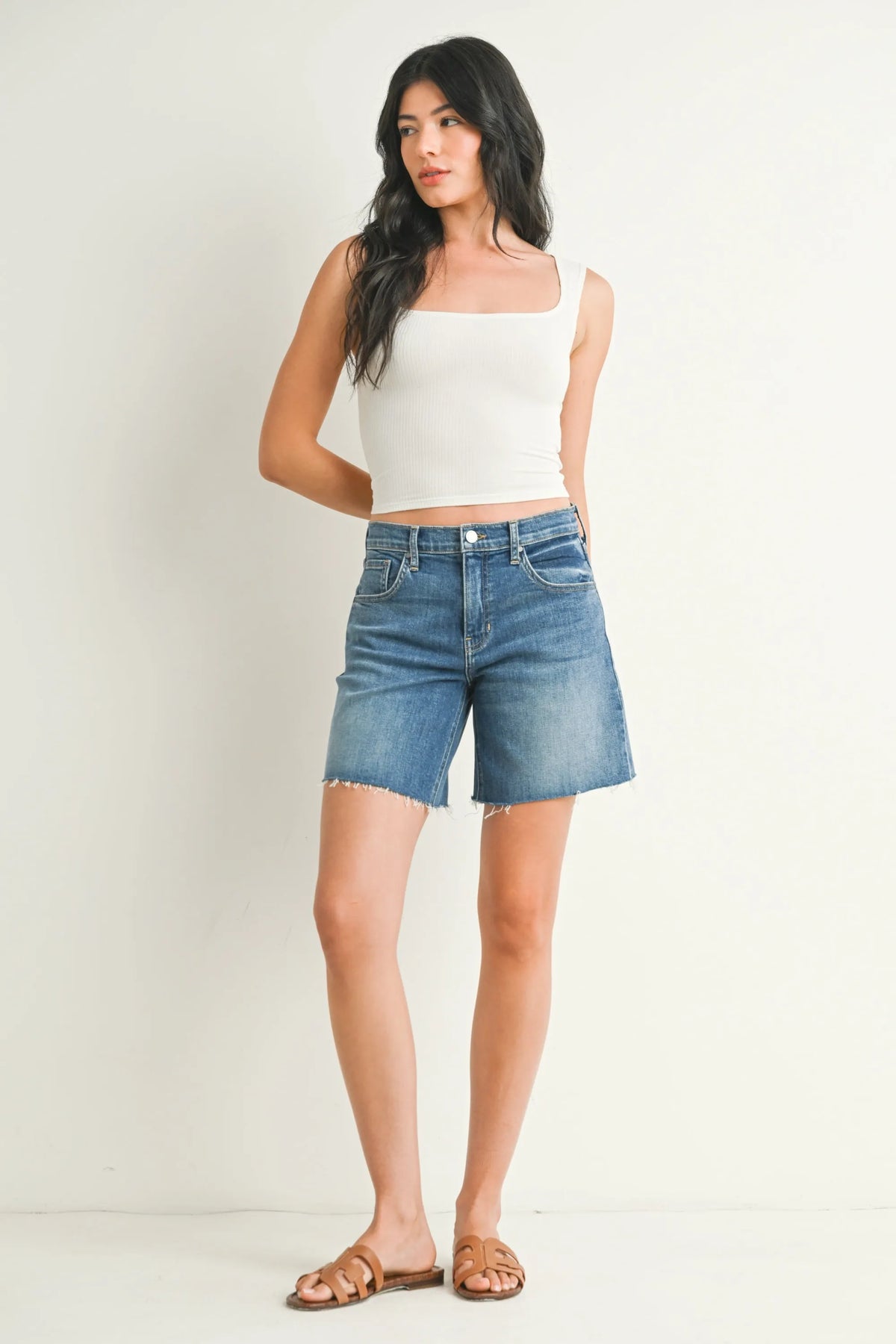 Mid rise bermuda denim jean short in medium blue wash with frayed hems and high-waisted fit