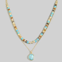A layered turquoise stone drop bead necklace with gold tones and a matching oval turquoise pendant