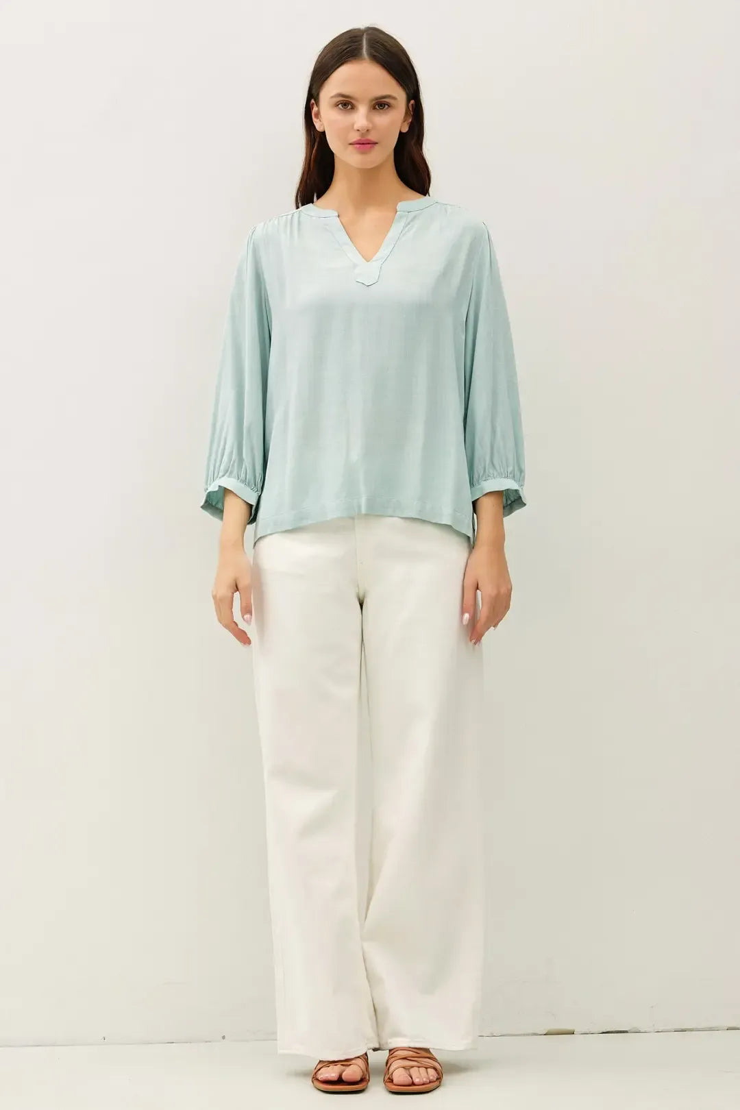 A light blue loose-fitting blouse with notched y-neck volume sleeve and three-quarter length sleeves