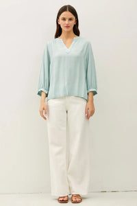 A light blue loose-fitting blouse with notched y-neck volume sleeve and three-quarter length sleeves