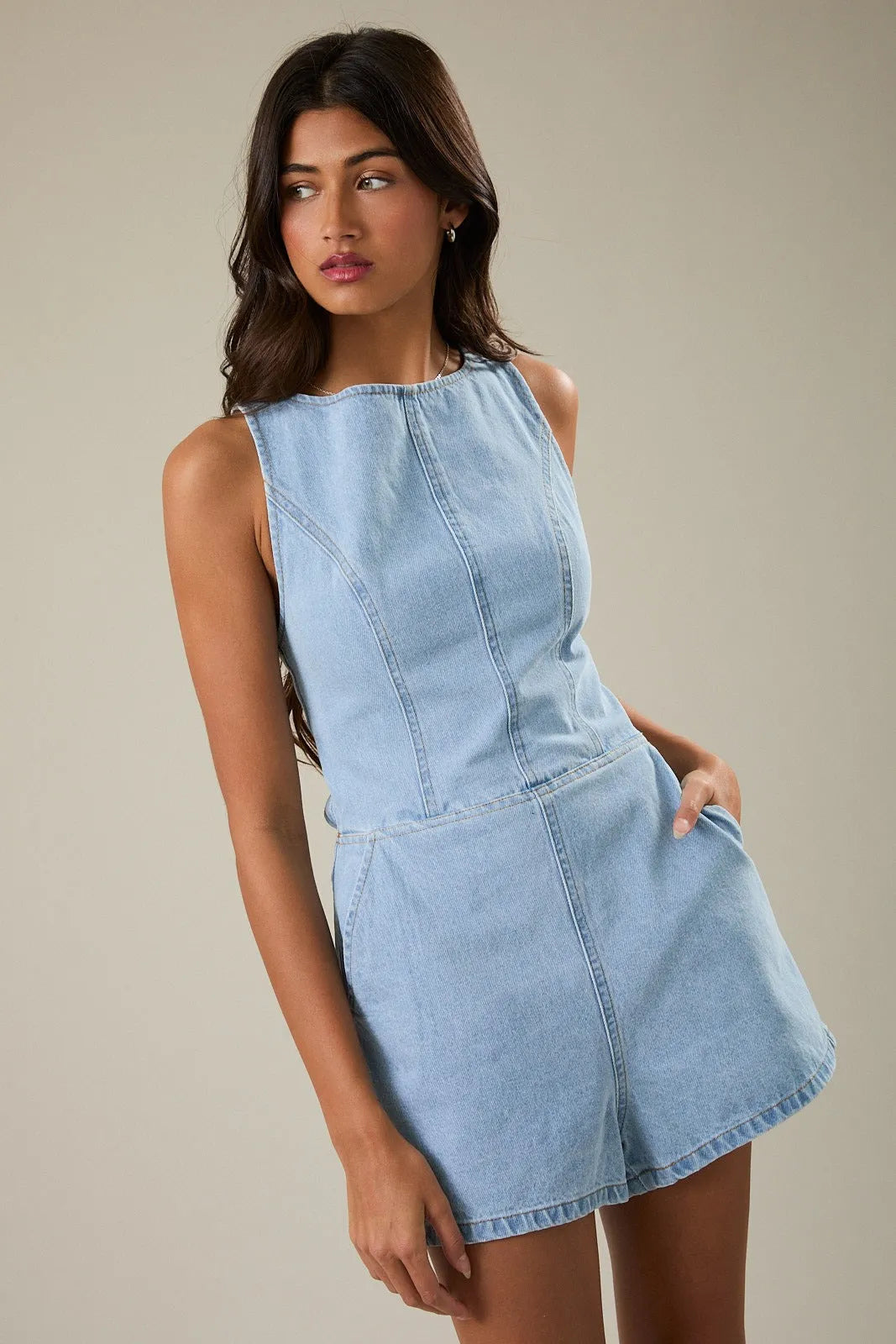 Light blue denim romper with boat neck tie, sleeveless design, high neckline, and front seam detailing