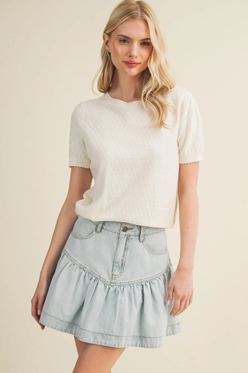 A light blue denim skirt with ruffled hem and front pockets paired with a starburst pointelle puff sleeve top