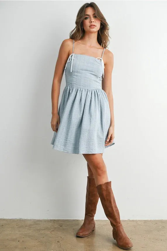 A light blue textured cotton polka dot flare mini dress with thin white strap fit tie straps and a flared skirt