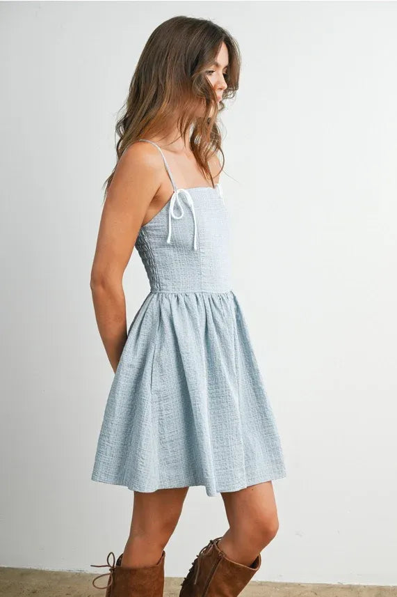 A light blue textured cotton polka dot flare mini dress with a square neckline and adjustable strap fit