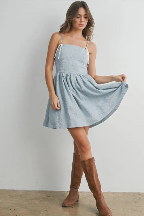 A light blue textured polka dot flare mini dress with thin spaghetti straps and a gathered waist strap fit