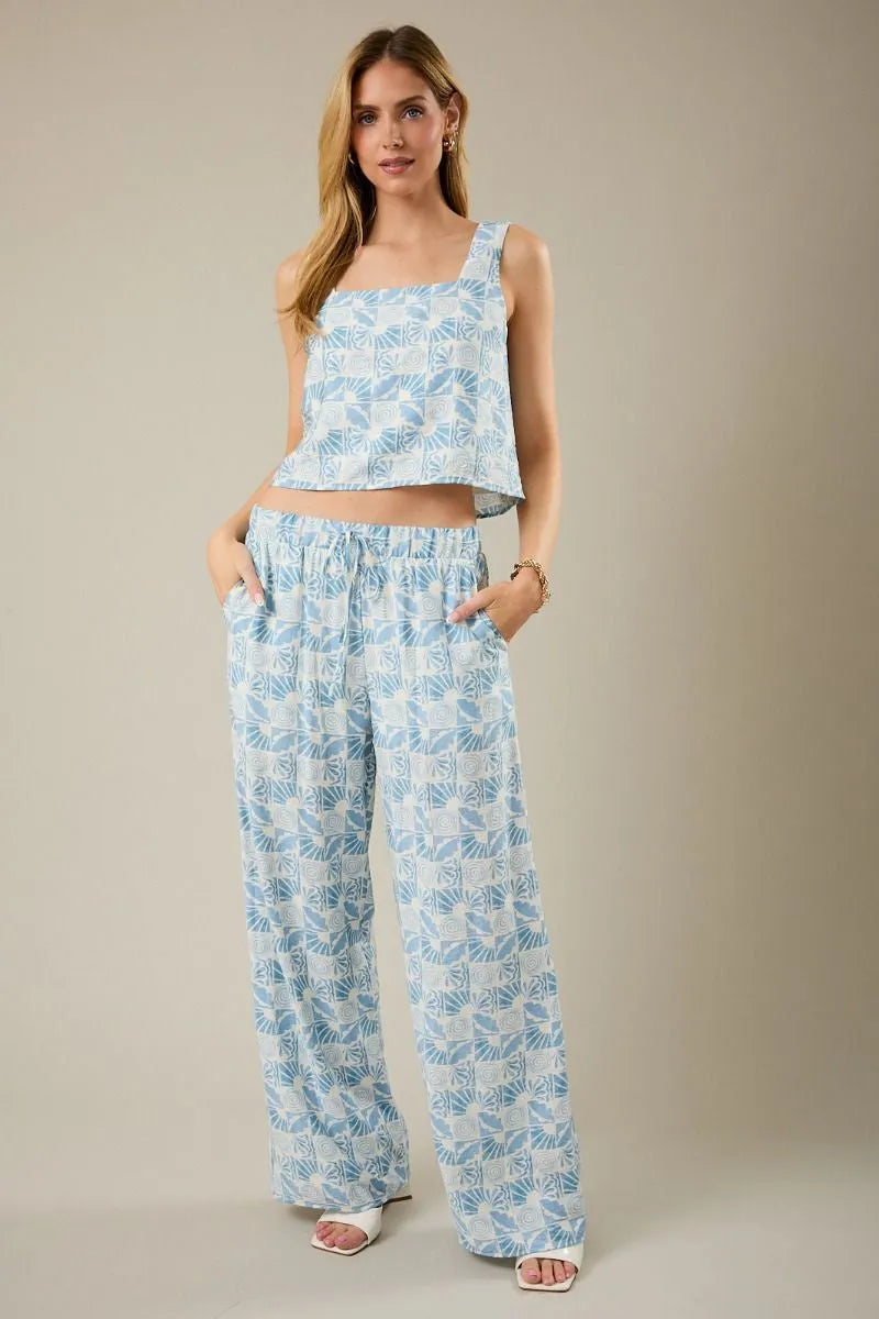 Light blue and white patterned wide-leg pants paired with a sleeveless square neck abstract print top in flowing fabric