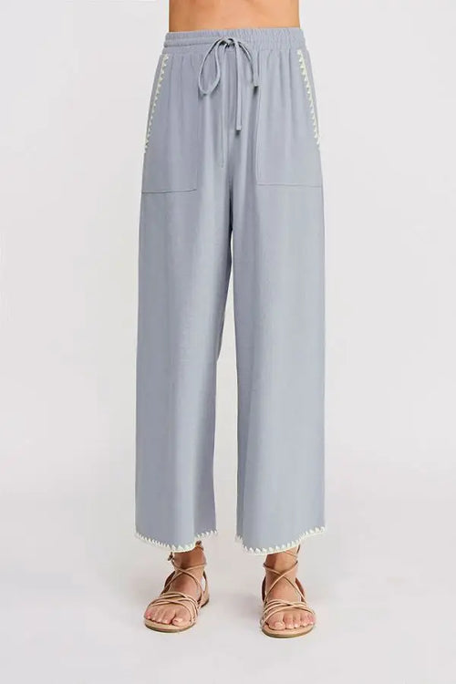 Light blue linen wide leg pant with elastic tie waist and white pom-pom trim along sides and hem