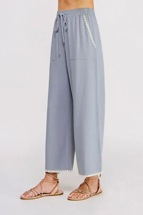 Light blue linen wide leg pants with elastic tie waist and white zigzag trim along side seam and hem