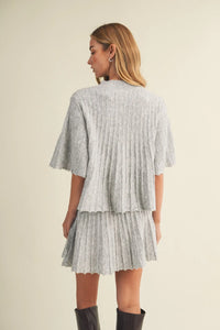 A light gray wide rib knit two-piece outfit with a cropped cape-style top and matching pleated skirt
