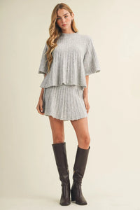 A light gray two-piece pleated dress set with tiered top and matching skirt paired with a wide rib knit pullover sweater