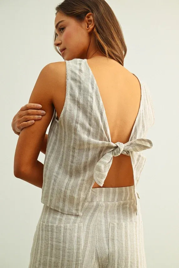 A light gray and white vertically striped jacquard linen twisted tie back top shown from the back side
