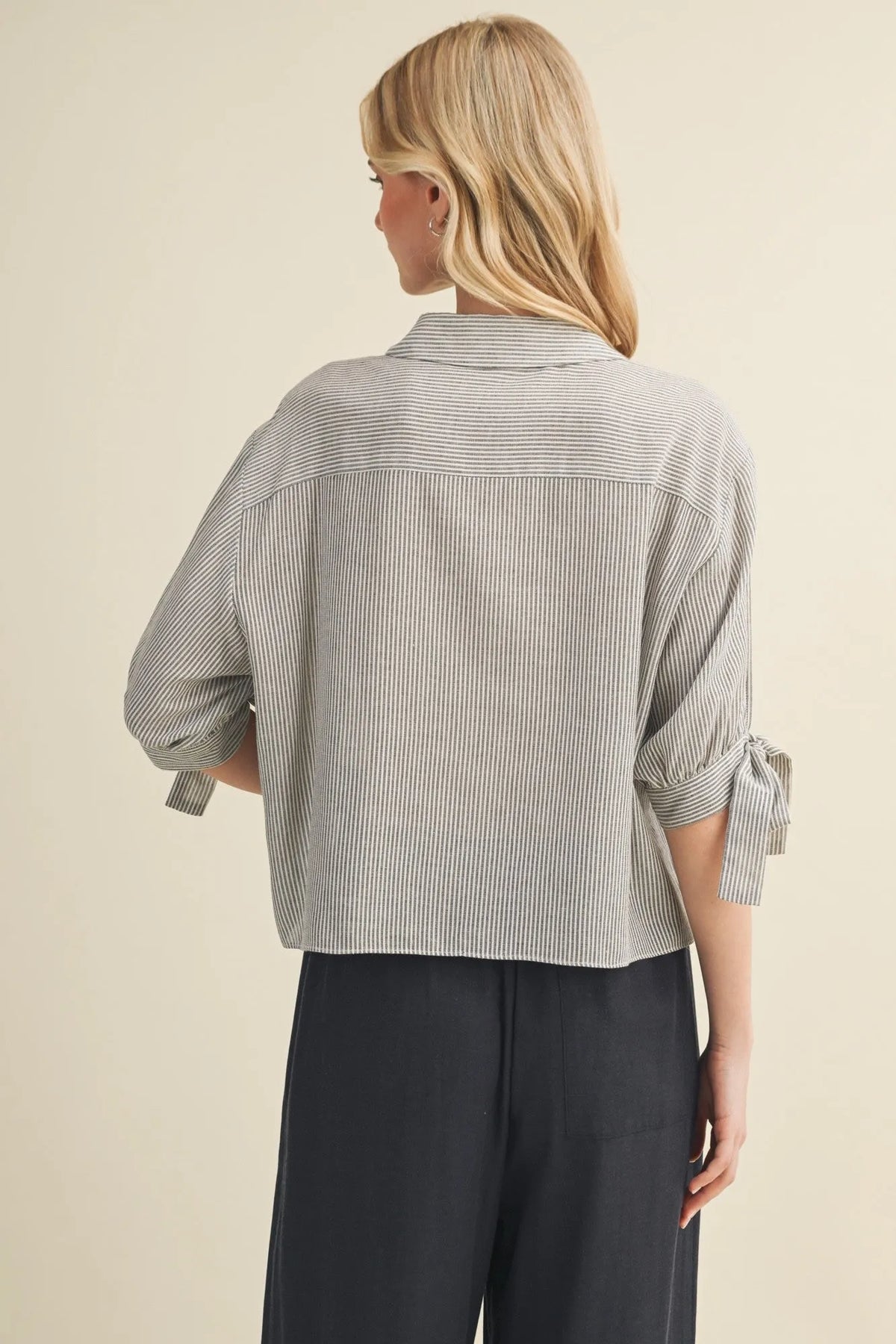 A light gray and white cotton striped tie cuff button front top with rolled-up sleeves tied in bows at the cuffs