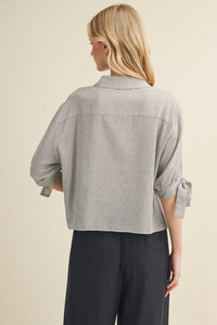 A light gray and white cotton striped tie cuff button front top with rolled-up sleeves tied in bows at the cuffs