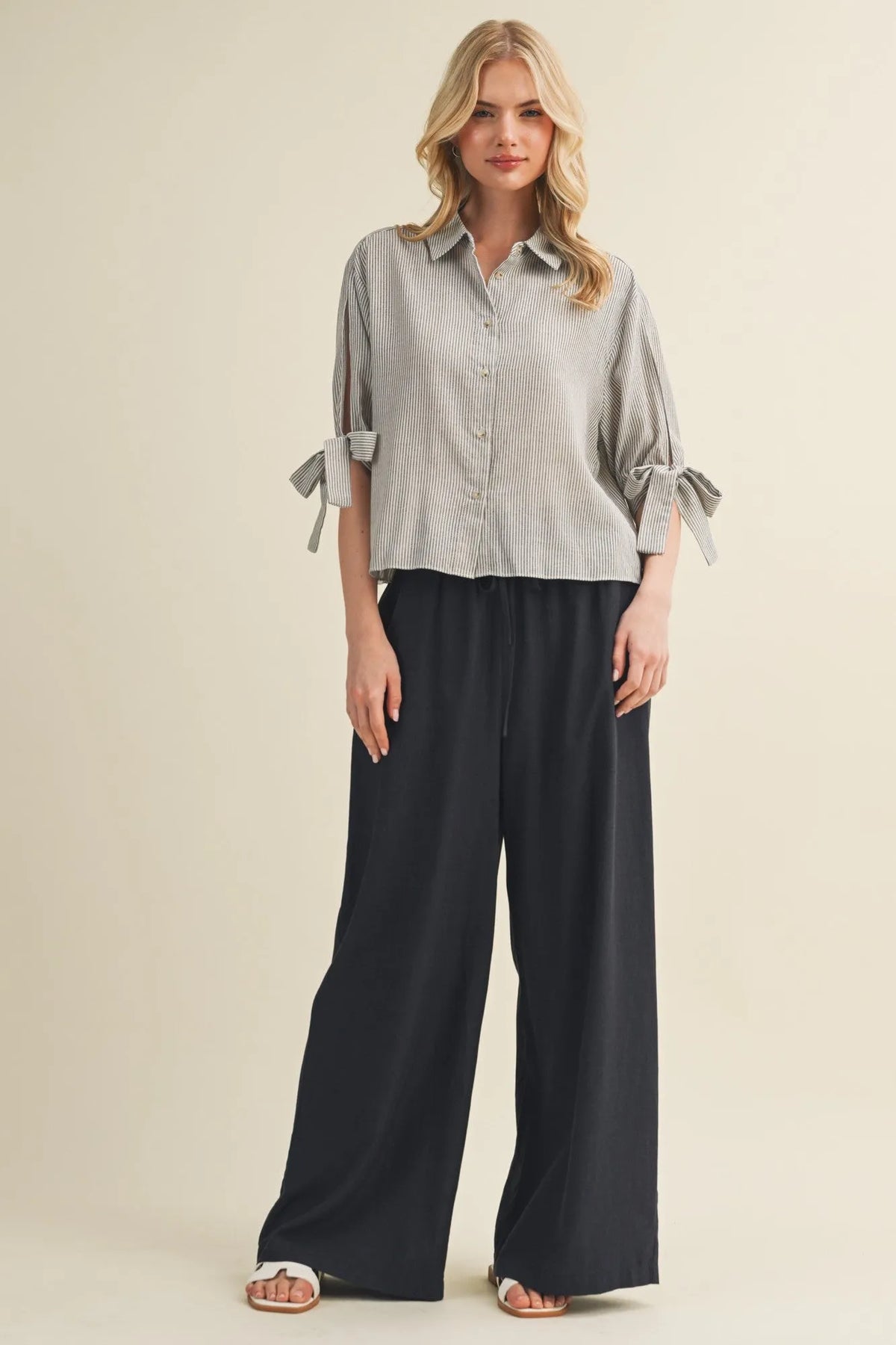 A light gray and white vertically striped tie cuff button front top with tied cuffs for a stylish look