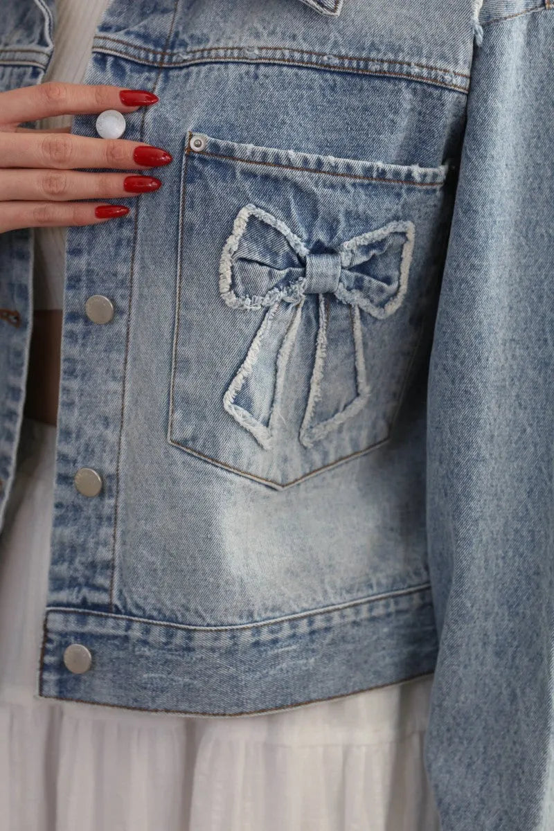 Light-wash oversized trucker denim jacket with decorative bow patch on the back pocket in a casual style
