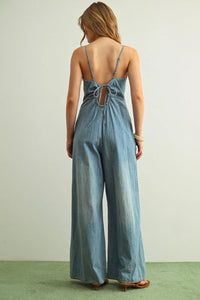Light-wash spaghetti strap chambray jumpsuit with thin straps and tied-back neckline shown from the back side
