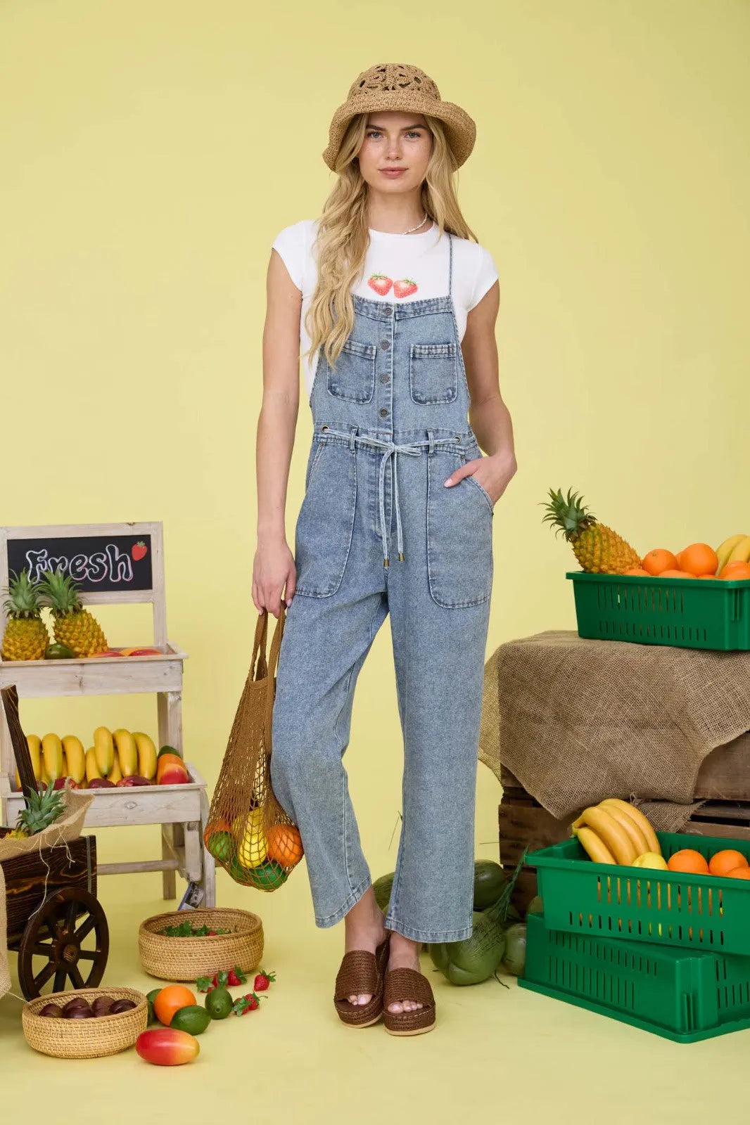 Light-wash denim washed spaghetti strap overalls with tie-front waist and front pockets in a casual summer outfit