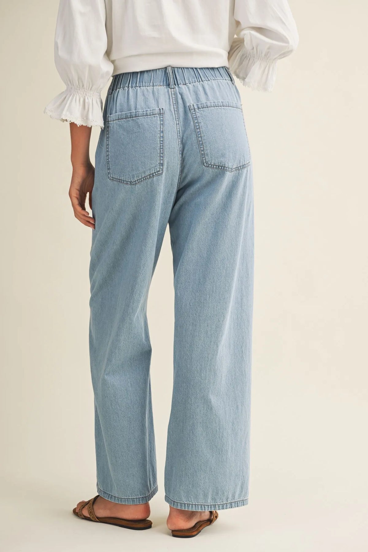 Light-wash relaxed denim pants with elastic drawstring waist and back pockets shown from the back side