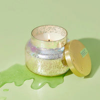 A lit mercury iridescent candle in an iridescent glass jar with speckled metallic finish and gold lid