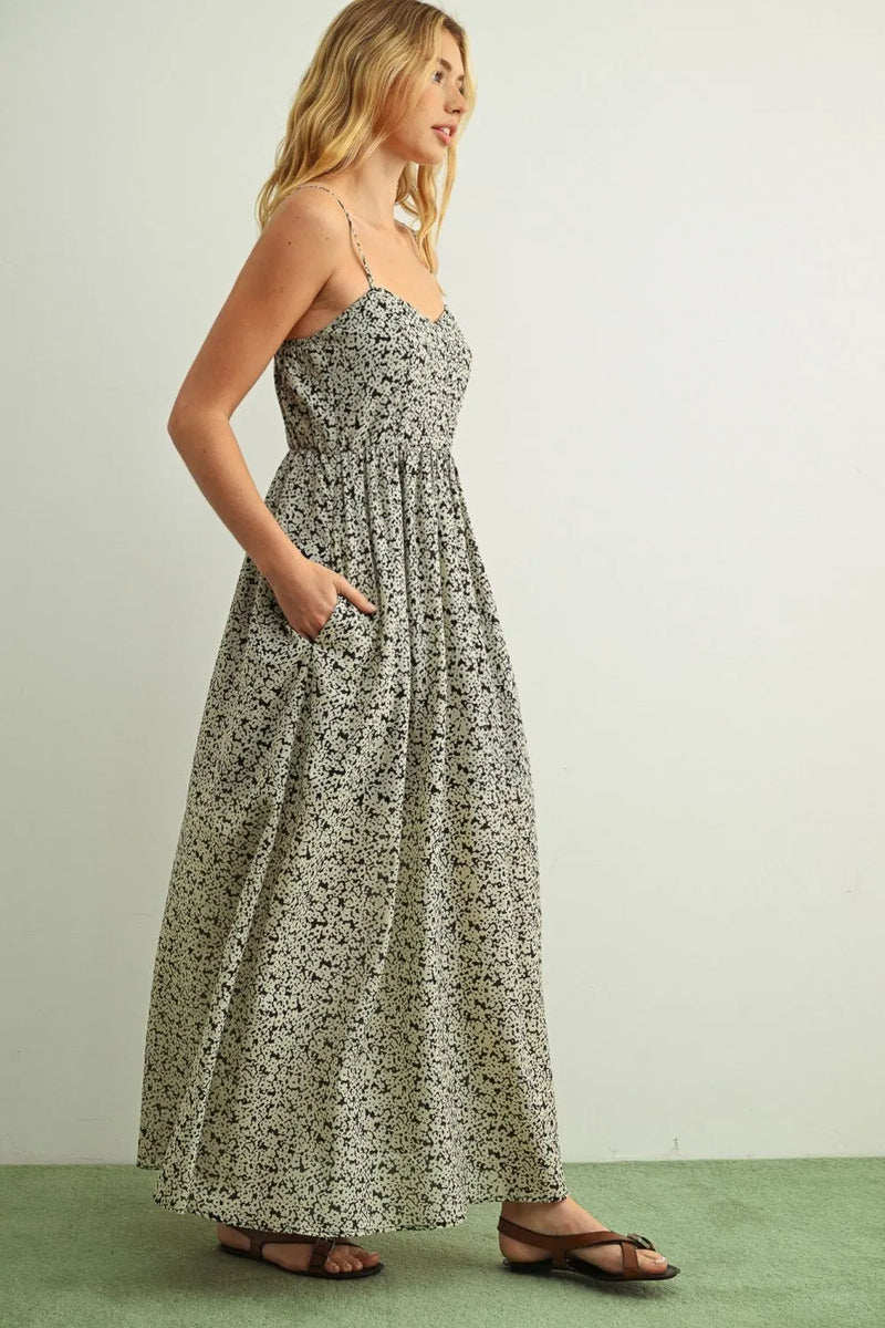A flowing long-sleeved floral print maxi dress in soft sage green fabric with delicate black floral patterns and spaghetti straps