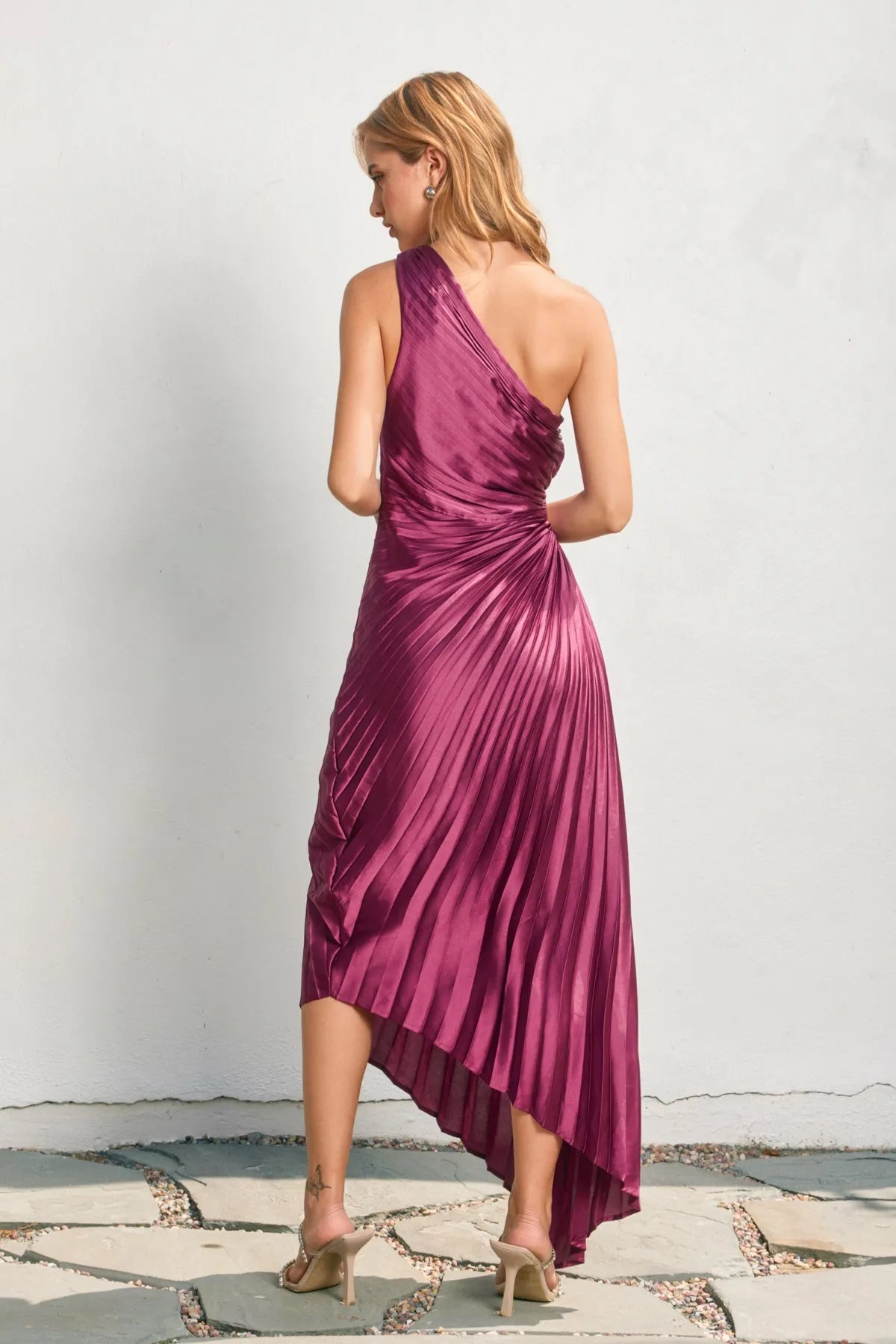 A shimmering magenta satin one shoulder asymmetrical pleated dress with a high-low hemline